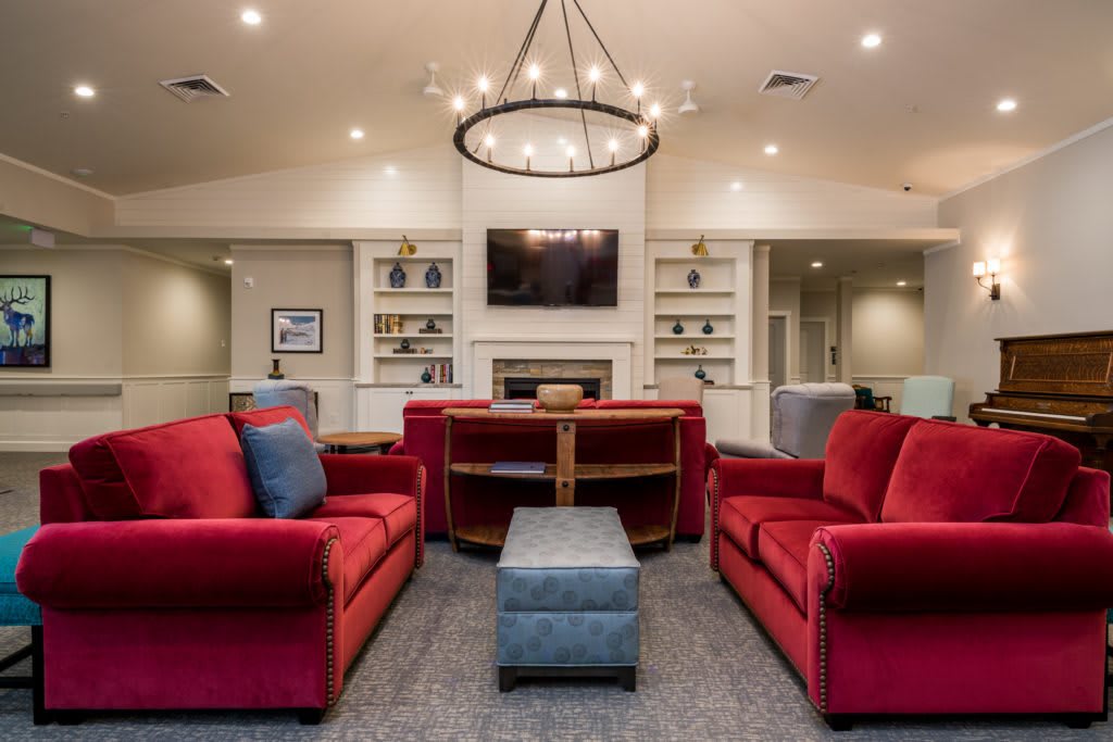 A modern living room featuring red sofas, a central chandelier, and a fireplace with a mounted TV.