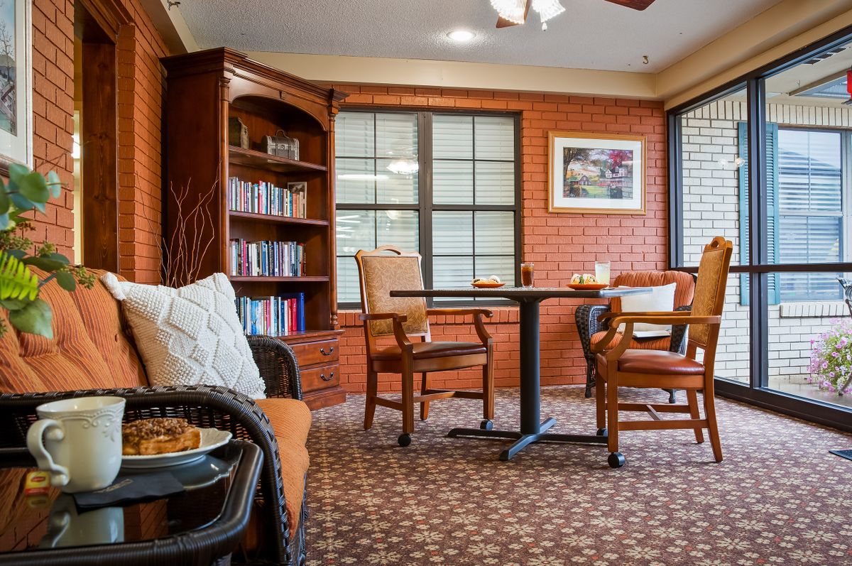 A cozy living room with a bookshelf, comfortable chairs, and a table by the window.