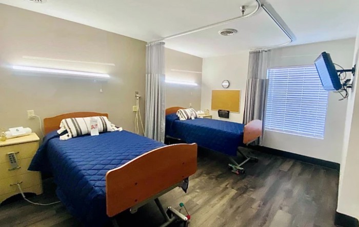A well-lit hospital room with two adjustable beds and privacy curtains.