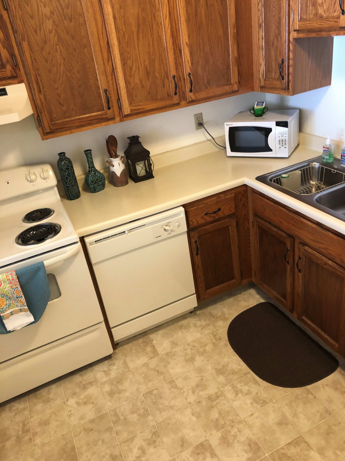 A cozy kitchen with wooden cabinets featuring a stove, microwave, dishwasher, and various decorative items on the countertop.
