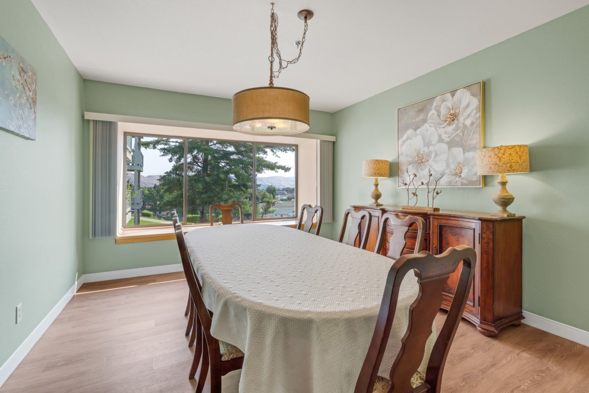 A spacious dining room with a long table, surrounded by wooden chairs, and a large window offering a scenic view.