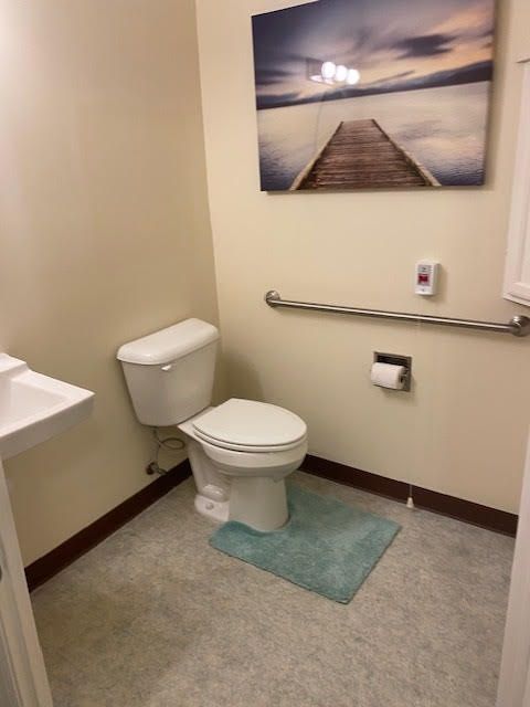 A clean and minimalistic bathroom featuring a toilet, sink, and wall-mounted artwork.