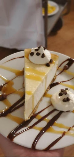 Indulge in a creamy slice of cheesecake, drizzled with caramel and topped with whipped cream and chocolate chips.
