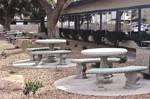 A tranquil outdoor space featuring several concrete picnic tables surrounded by gravel and greenery.