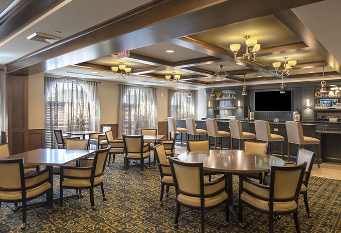 A cozy restaurant interior featuring multiple tables and chairs, with a bar area in the background.
