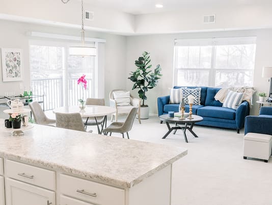 A bright and modern open living room and dining area with a blue sofa and minimalist decor.