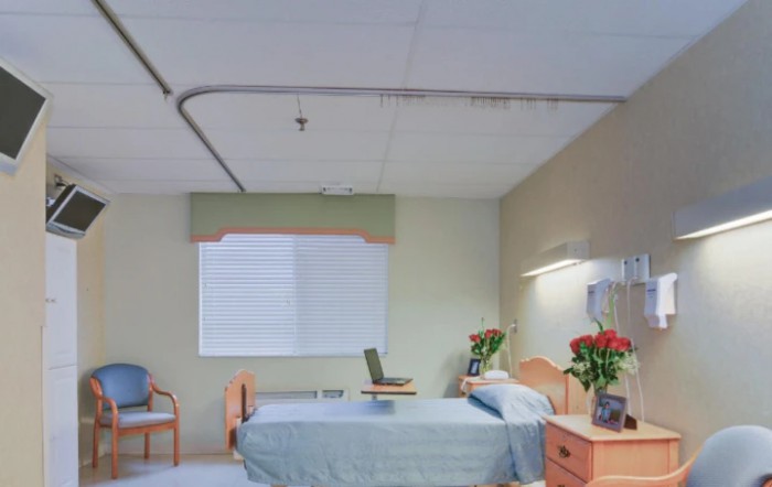 A well-lit hospital room with a bed, flowers on the side table, and a chair near the window.