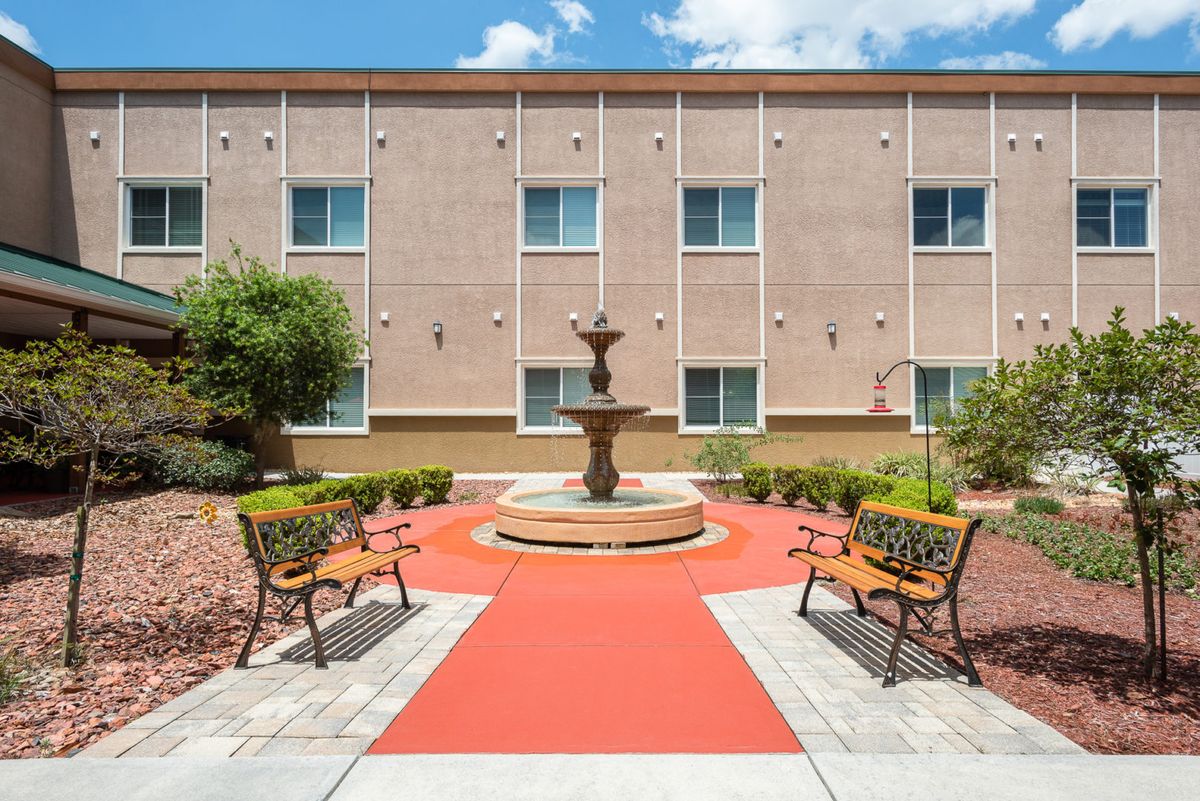 A tranquil courtyard featuring a central fountain, surrounded by benches and a bright red pathway.