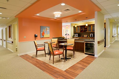 A cozy interior dining area with orange walls, featuring a small kitchenette and wooden furniture.