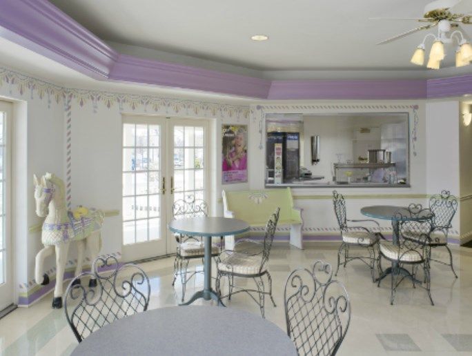 A cozy cafe interior with round tables and wrought iron chairs, featuring large windows allowing natural light to fill the room.