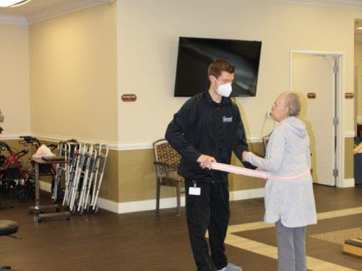 A healthcare worker assists an elderly woman during a physical therapy session in a warm and welcoming environment.