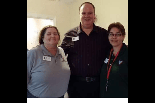 Three people posing for a group photo indoors.