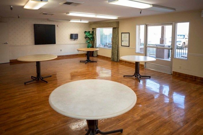 An empty room with several round tables and a wooden floor, brightly lit by natural and artificial light.