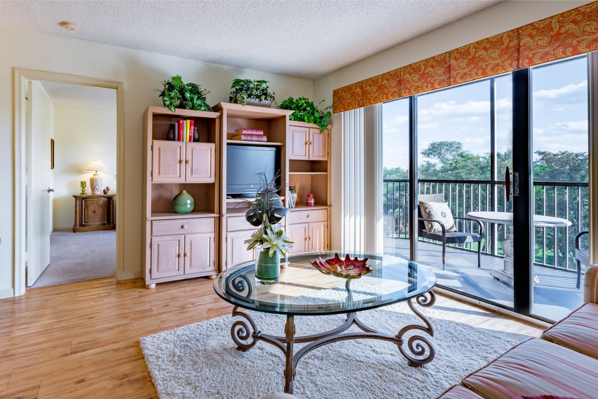 A cozy living room with a glass coffee table, entertainment center, and sliding doors leading to a balcony.