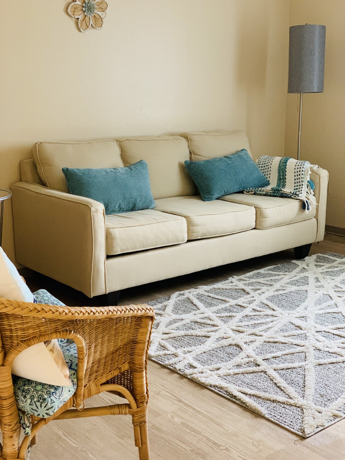 A cozy living room featuring a beige sofa with blue cushions, a geometric-patterned rug, and a wicker chair.