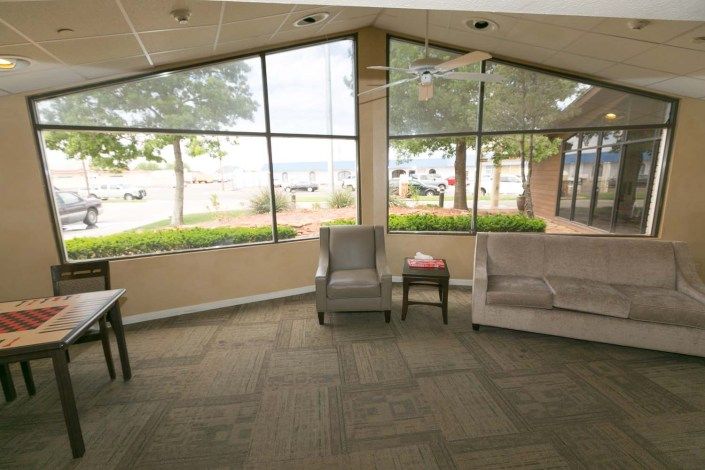 A bright waiting room with chairs and a sofa near large windows letting in natural light.