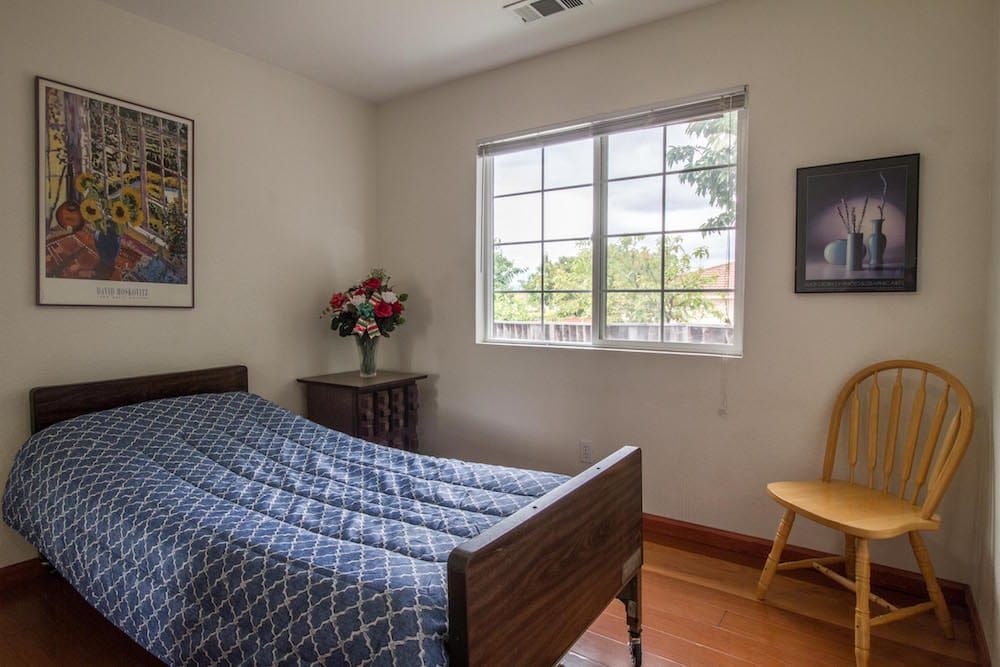 A cozy bedroom with a large window, wooden furniture, and natural lighting.