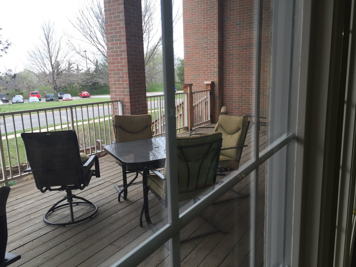 A view of a porch with outdoor chairs and a table seen through a window.