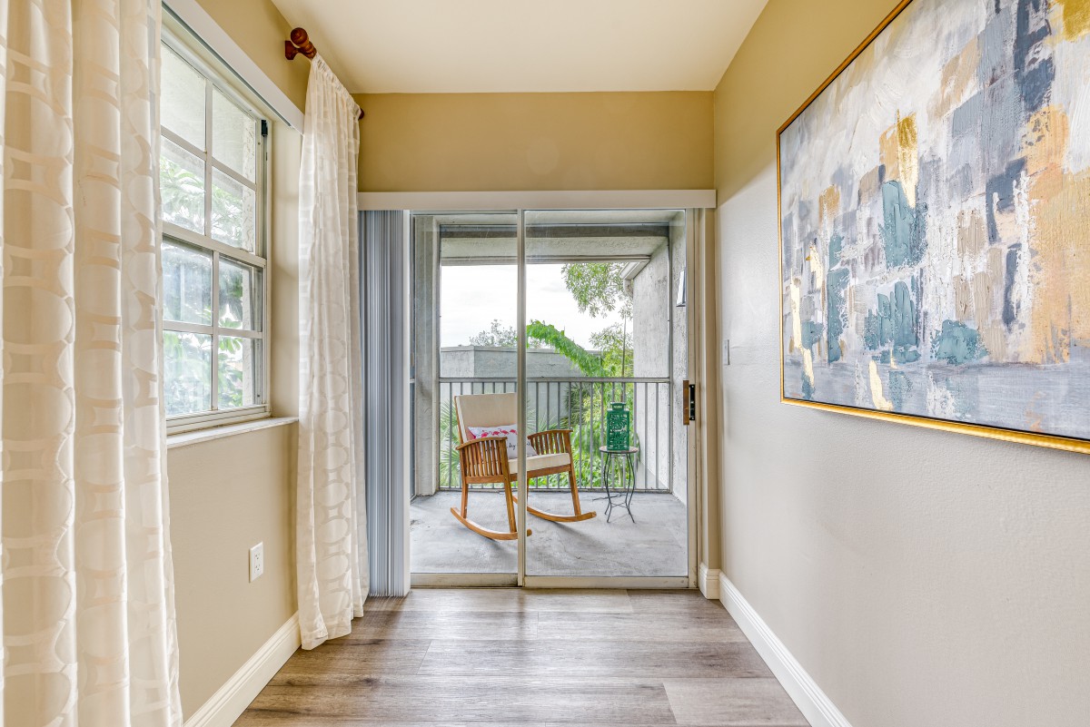 Bright room with a sliding glass door leading to a cozy balcony area featuring chairs and a table.