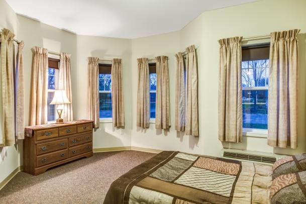 A cozy bedroom with multiple windows, a bed, and a dresser.