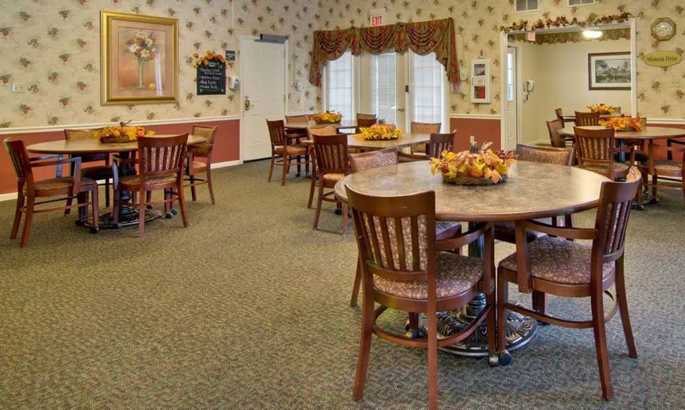 A cozy dining room with tables and chairs, decorated with floral arrangements and warm lighting.