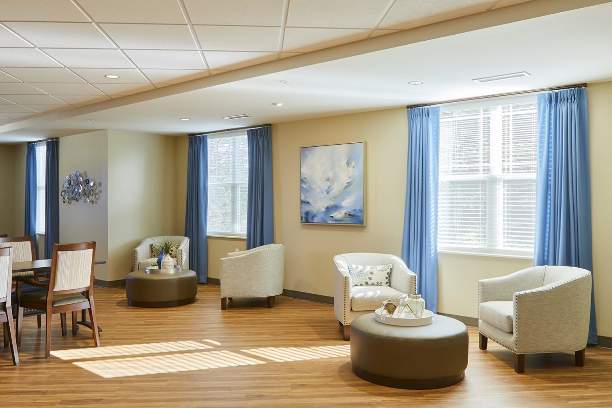 A cozy waiting room featuring comfortable seating, large windows with blue curtains, and a calming piece of artwork on the wall.