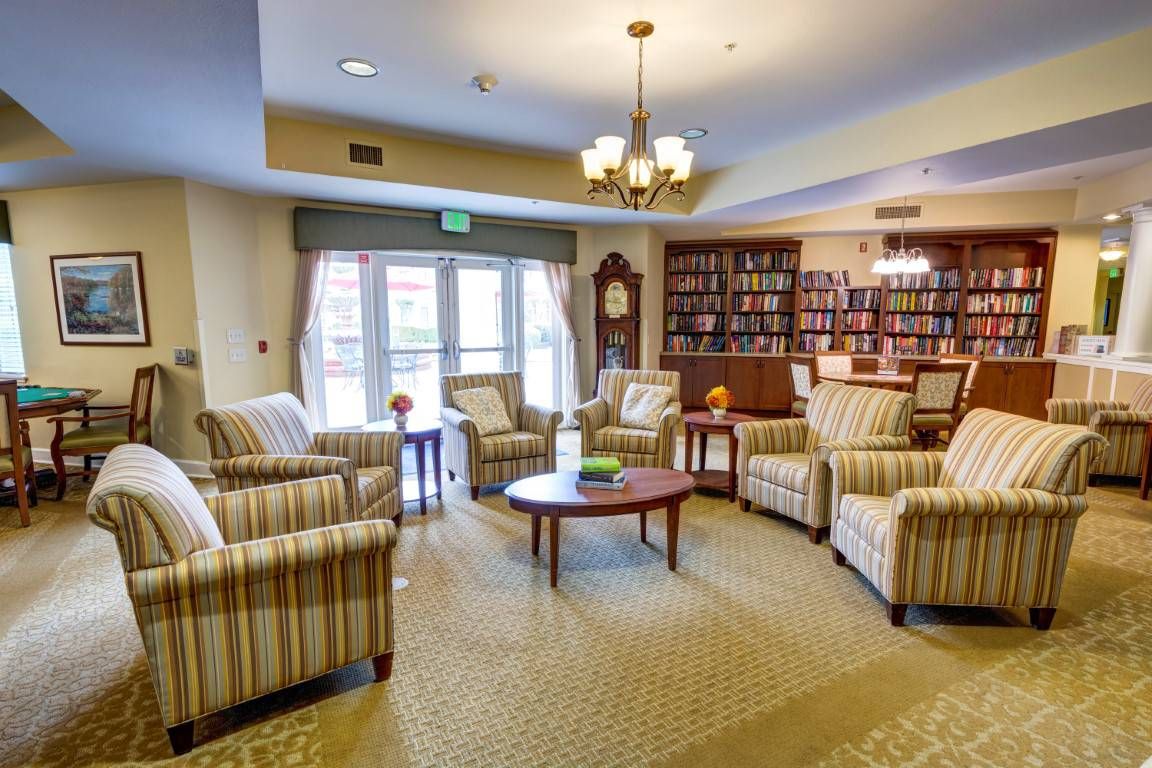A cozy living room with armchairs and bookshelves, featuring a chandelier and a carpeted floor.