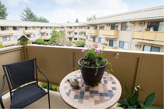 A cozy apartment balcony with a table and potted plant overlooking a residential complex.