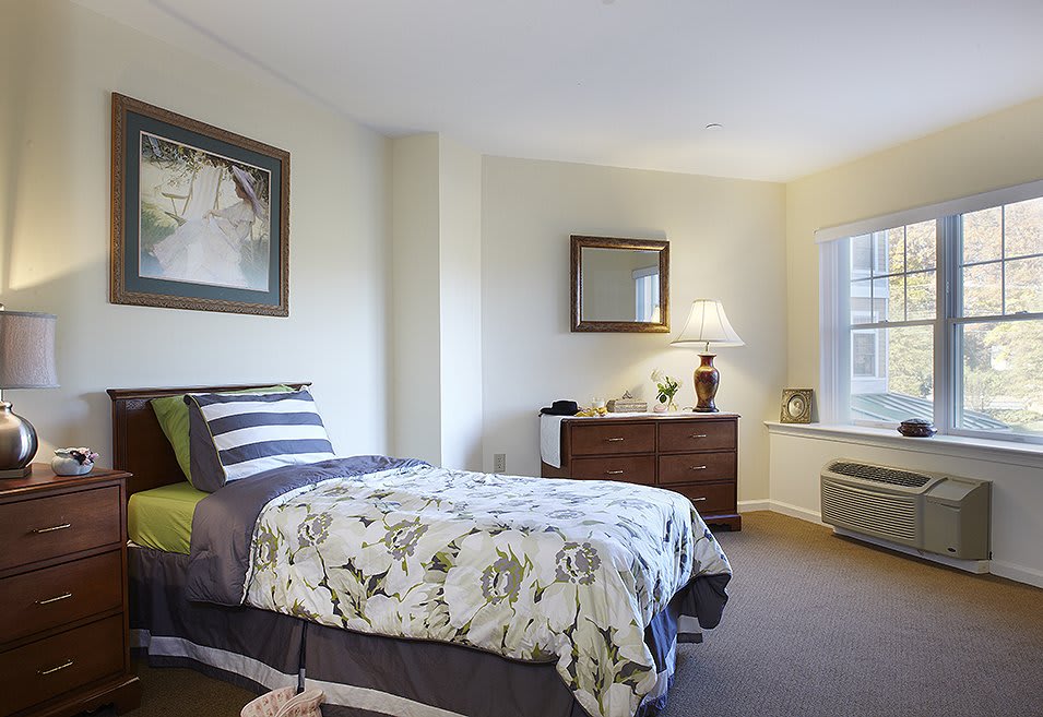 A cozy bedroom with a single bed, decorative pillows, and a dresser topped with a lamp.
