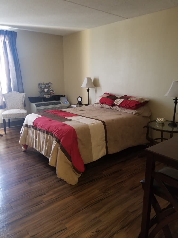 A cozy bedroom with a neatly made bed, bedside lamps, and wooden flooring.