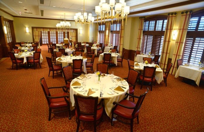 An elegant dining room setup with neatly arranged tables and chairs, illuminated by chandeliers.