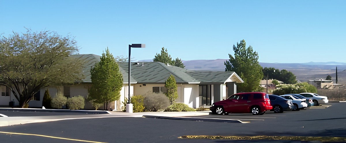 A suburban house with a car parked in front, surrounded by trees on a clear day.