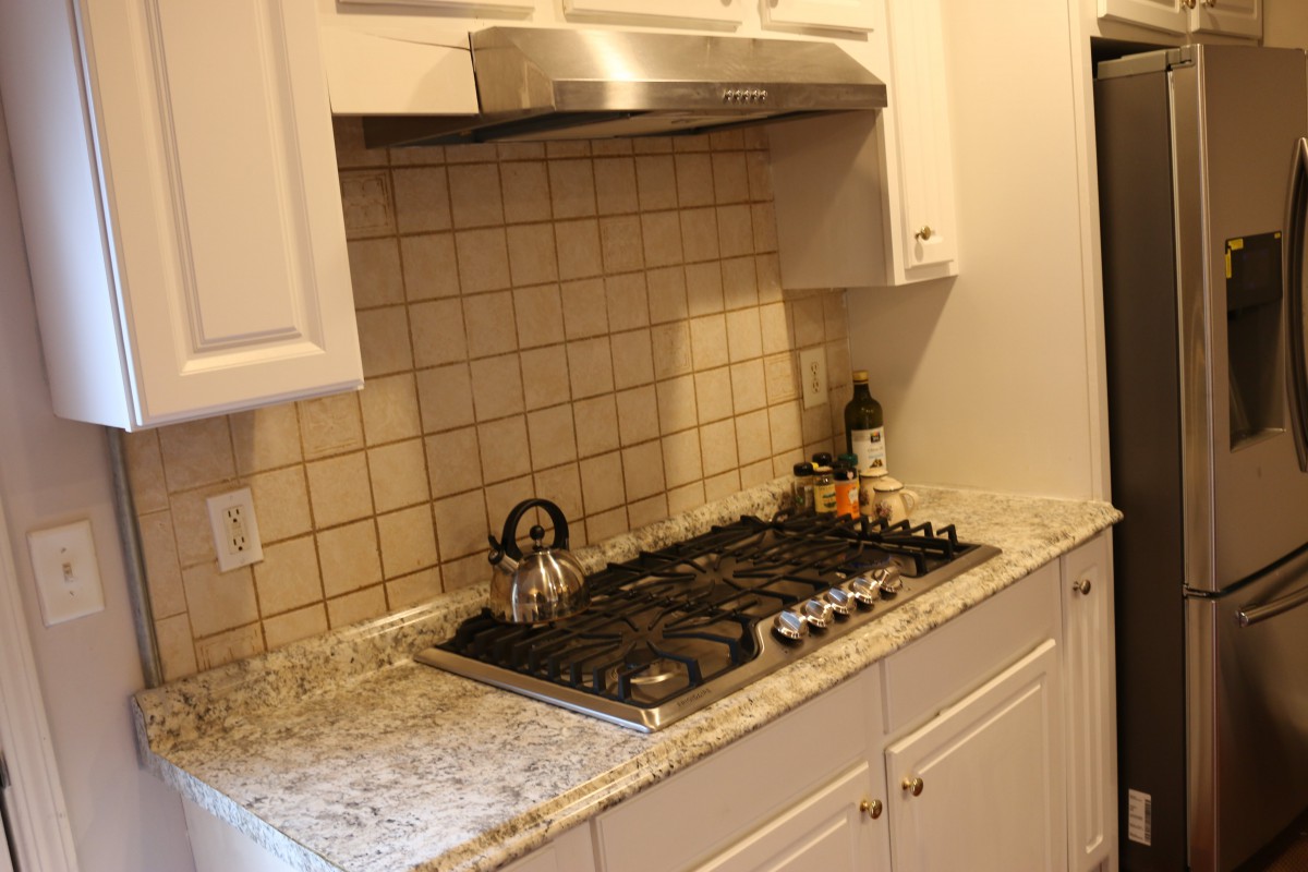 A kitchen setup featuring a gas cooktop with a kettle, tiled backsplash, and white cabinets.