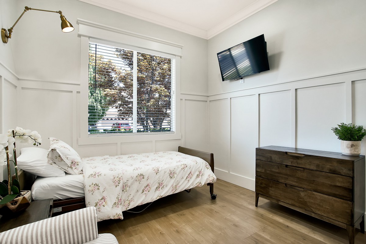 A modern bedroom with a single bed, wall-mounted TV, and a large window providing natural light.