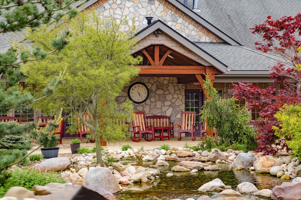 A charming house with a stone facade features a tranquil garden and pond, complemented by inviting rocking chairs on the porch.