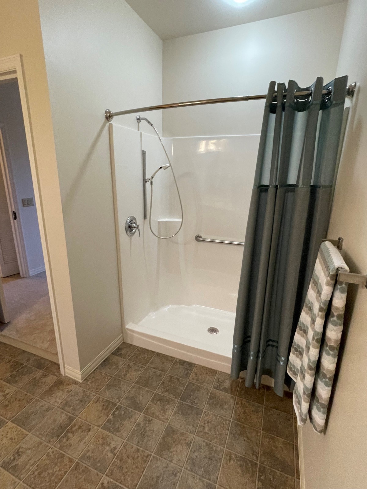 A bathroom with a curved shower featuring grab bars and a towel rack.