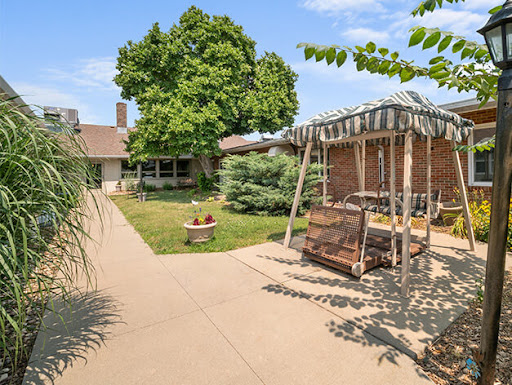 A serene outdoor space featuring a swing under a canopy, surrounded by lush greenery and a sunny sky.