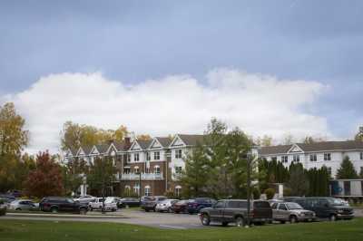 A view of a building with a parking lot in front, surrounded by trees under a cloudy sky.