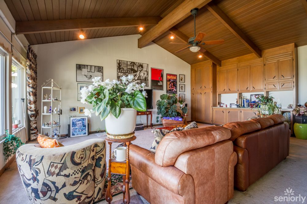 A cozy living room with a leather couch, wooden ceiling, and various artworks.