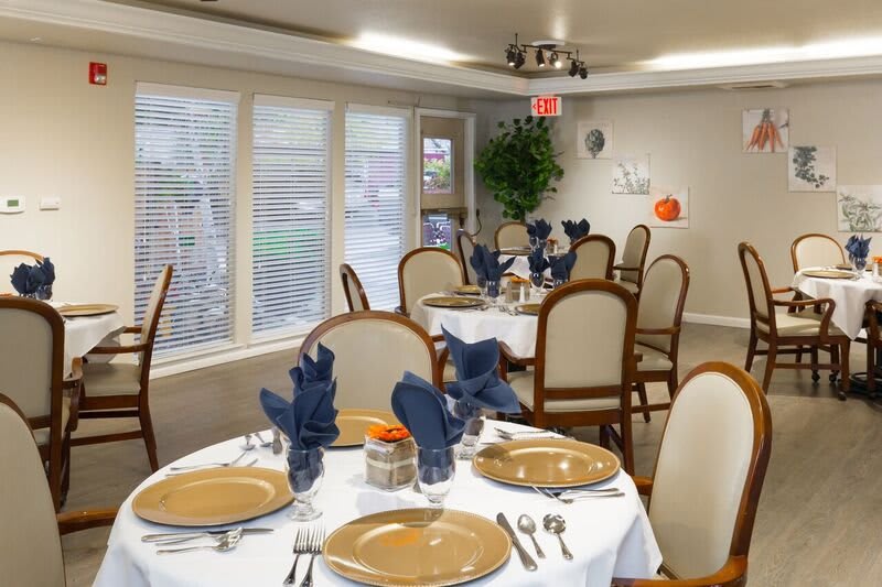 An elegantly set dining room with tables prepared for guests, featuring blue napkins and arranged silverware.