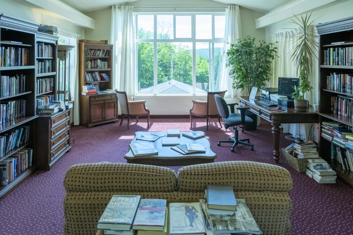 A cozy office space with bookshelves, desks, and ample natural light from a large window.