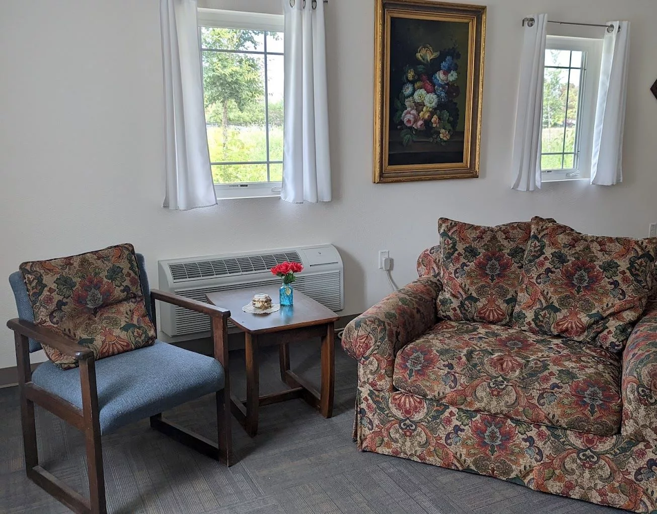 A cozy living room corner with a floral-patterned armchair, a small table, and a painting on the wall.