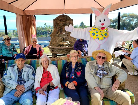 A group of seniors sitting together outdoors, accompanied by a person in an Easter bunny costume.