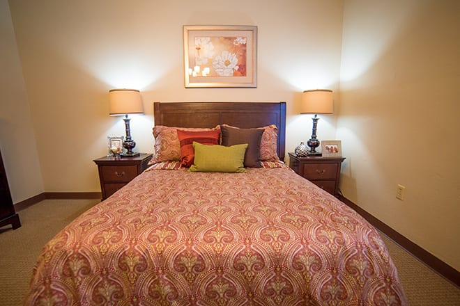 A cozy bedroom with a neatly made bed, flanked by two lamps on nightstands.