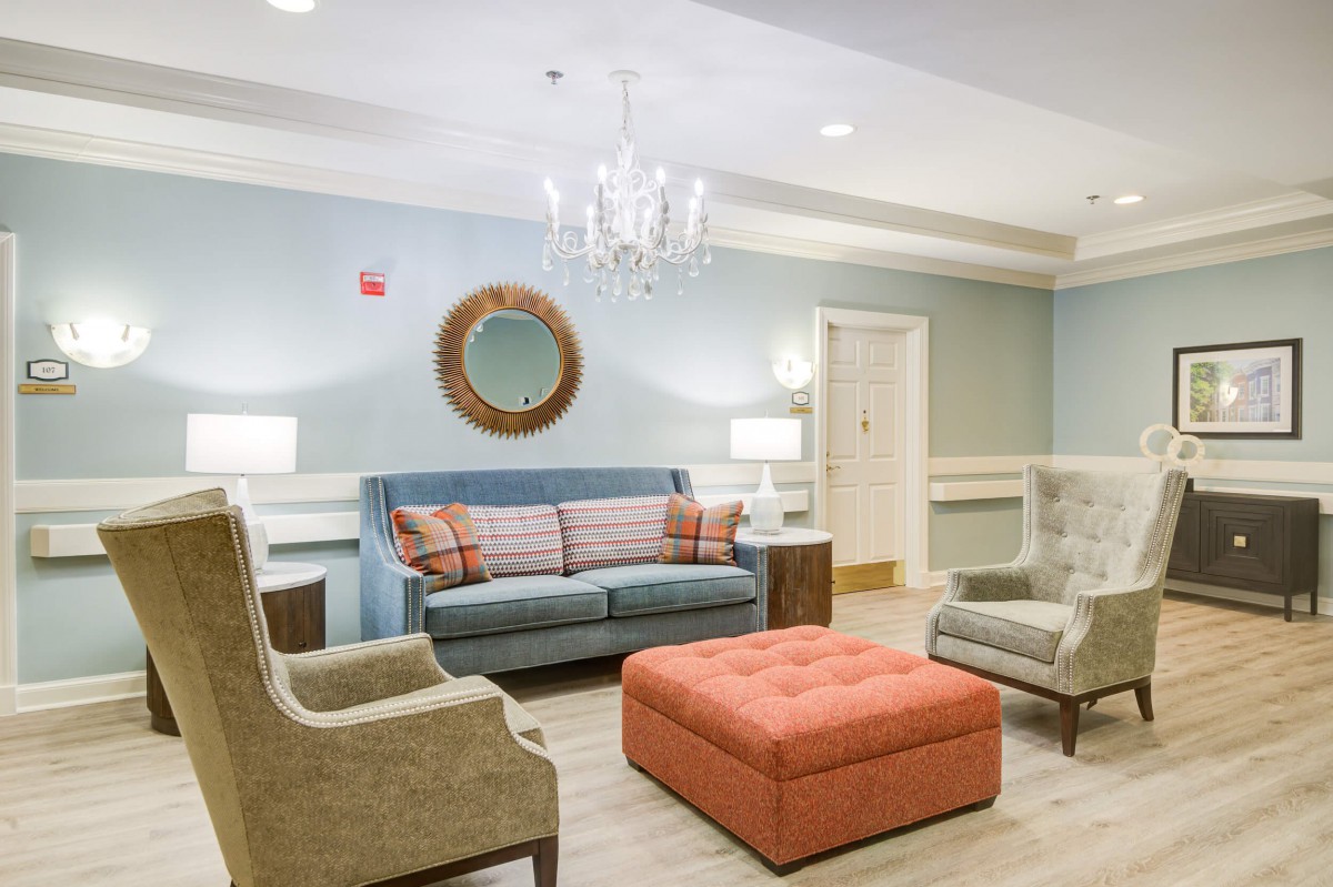 A cozy living room with a light blue sofa, orange ottoman, and elegant chandelier.