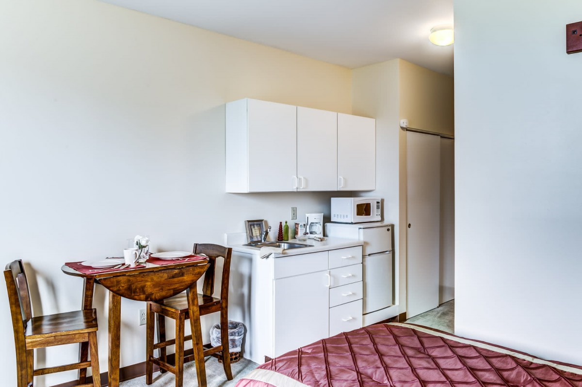 A compact kitchen area in an apartment with a small dining table, chairs, and essential appliances.