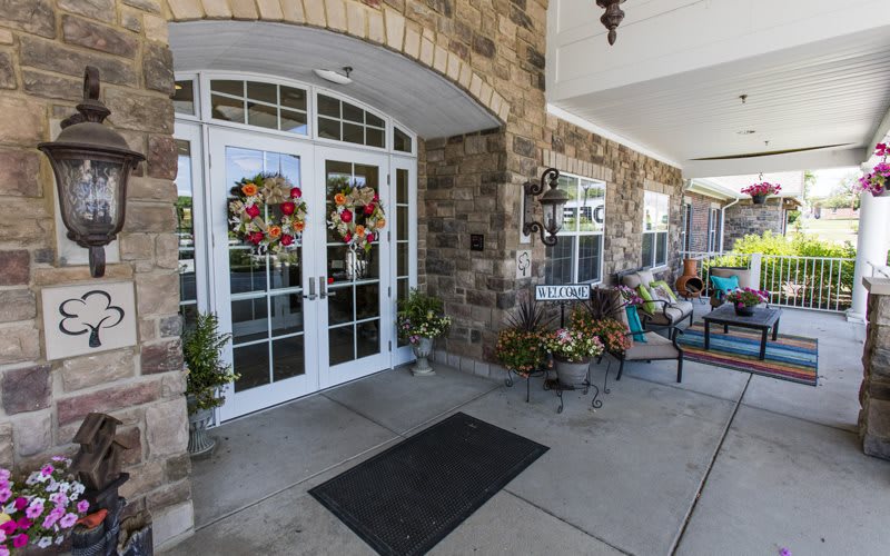A welcoming entrance with double doors adorned with colorful wreaths and outdoor seating surrounded by decorative plants.