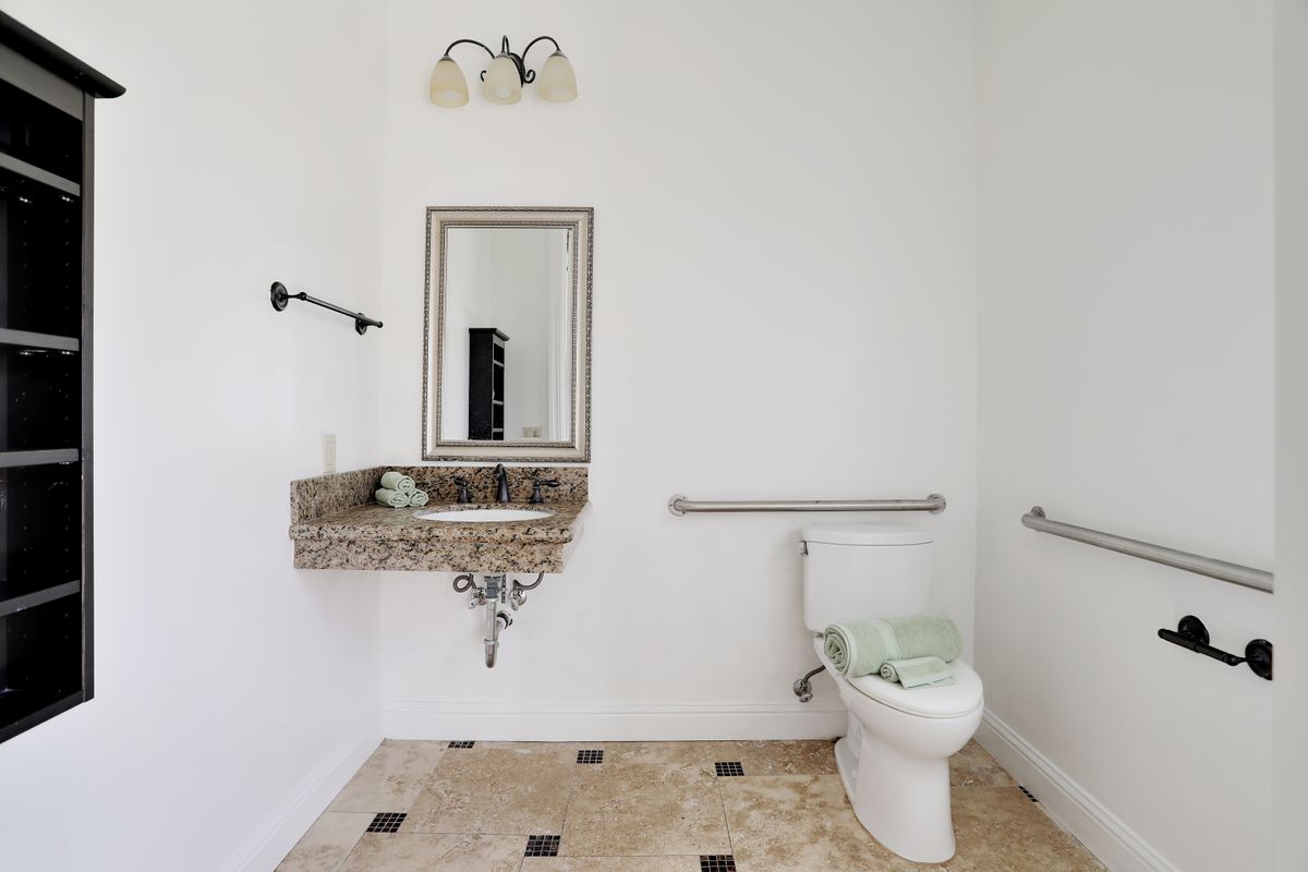 A modern bathroom with a granite sink, toilet, and stylish mirror.