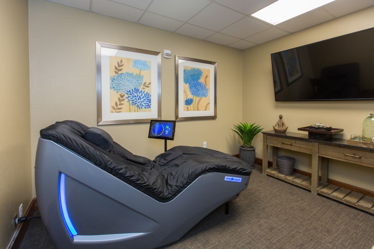 A modern therapy room featuring a sleek massage chair, abstract art, and calming decor.