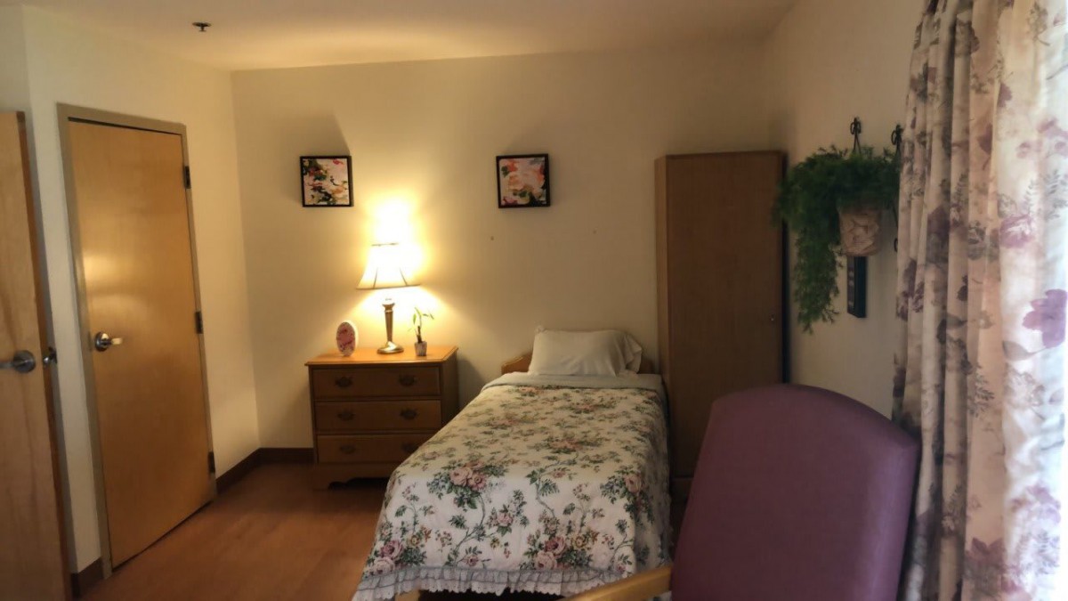A cozy bedroom with a single bed, lamp, dresser, and wardrobe.